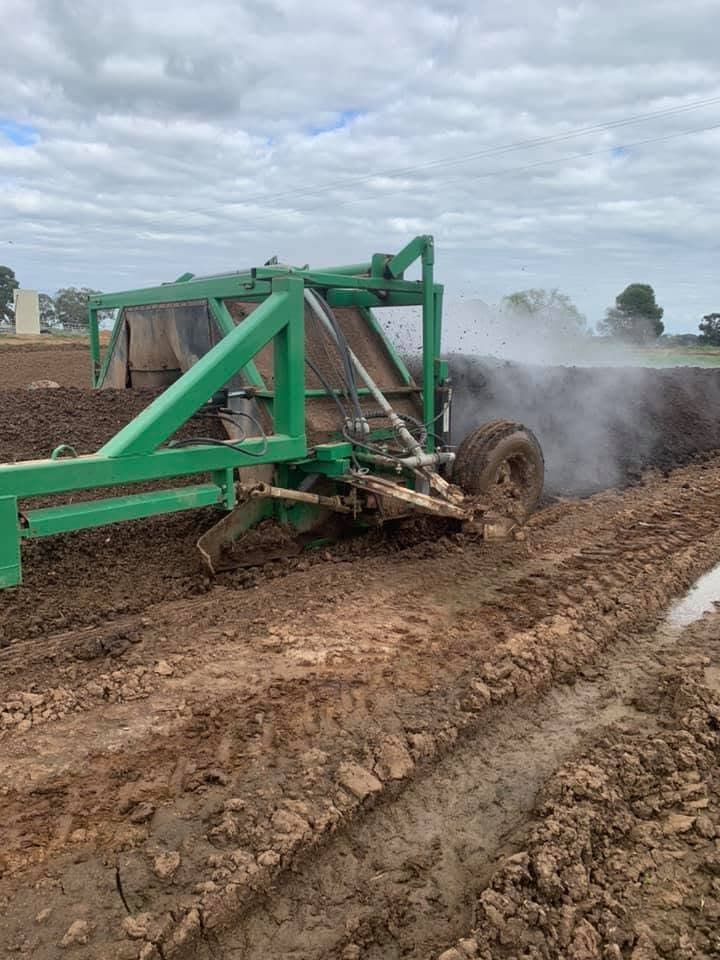 Compost turner processing a windrow with steam rising